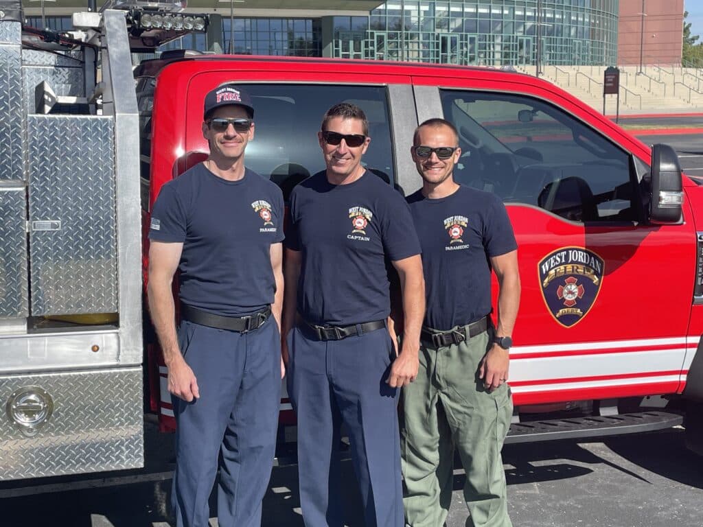 three west jordan firefighters stand in front of a vehicle smiling while wearing sunglasses before embarking on a journey to california