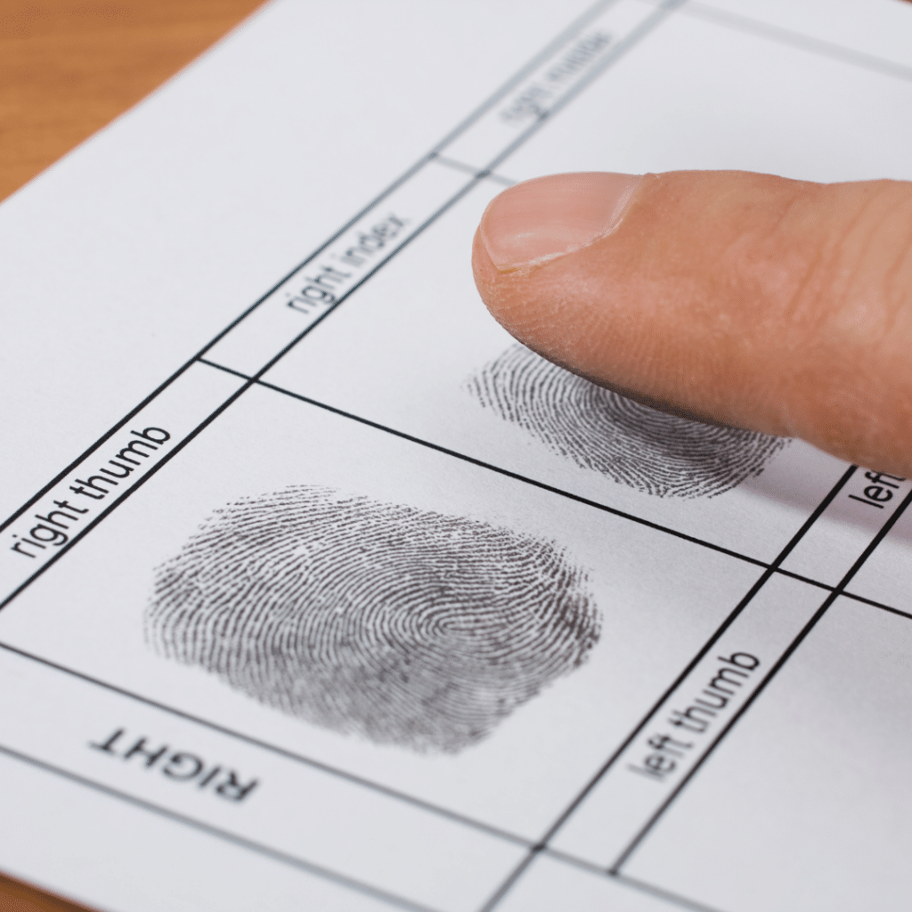 A persons finger is pressing down on a fingerprint form, creating an impression in the designated area labeled right index. Nearby, theres a completed fingerprint labeled right thumb, both on a white paper sheet.