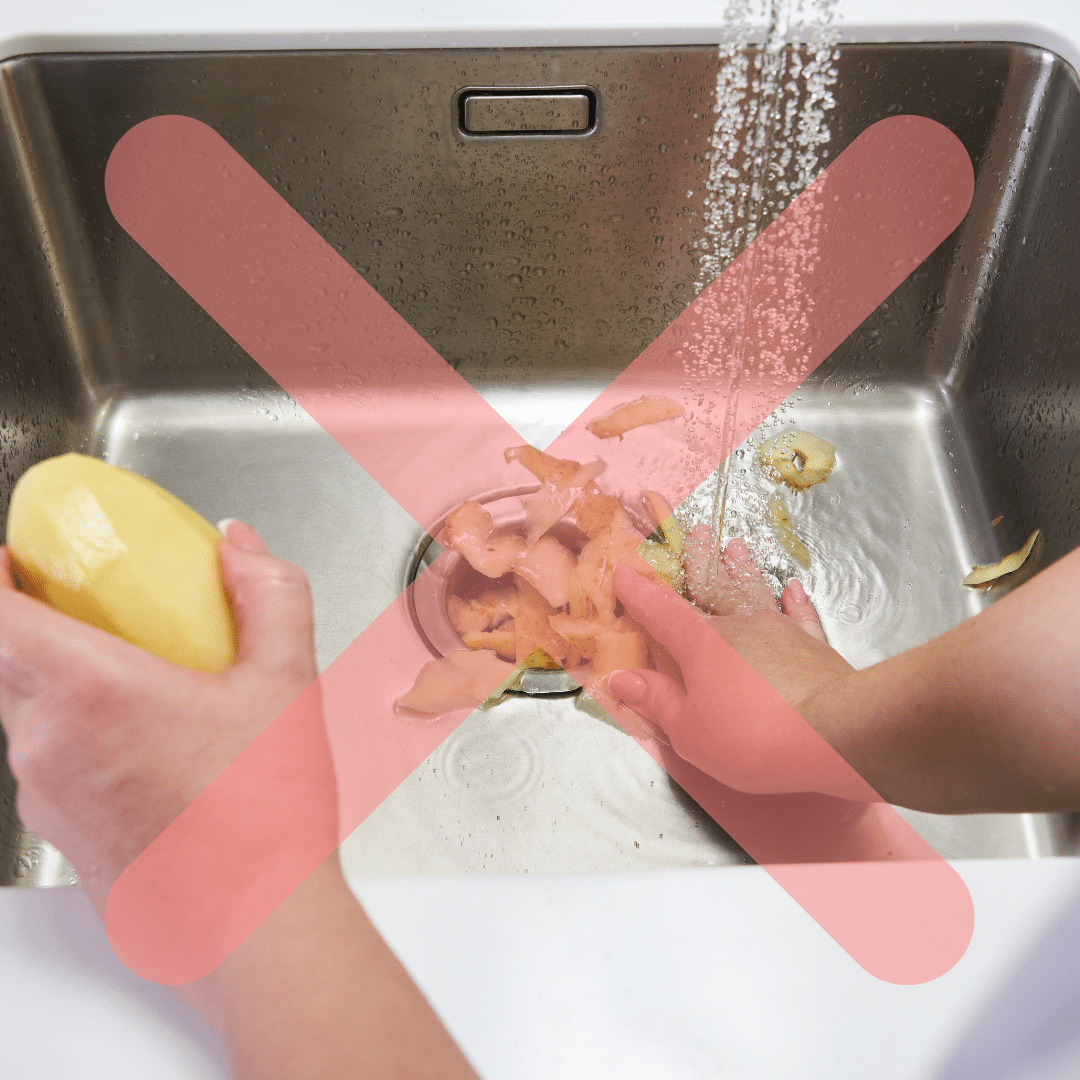 A person peels a potato over a sink with water running. Potato peels are directed into the drain. A large red X overlays the image, indicating not to dispose peels in the sink.