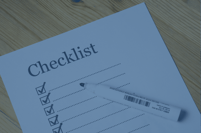 A paper with the title Checklist lies on a wooden surface. Six checkboxes are visible, each with a checkmark. A white pen rests on the paper, angled slightly to the right.