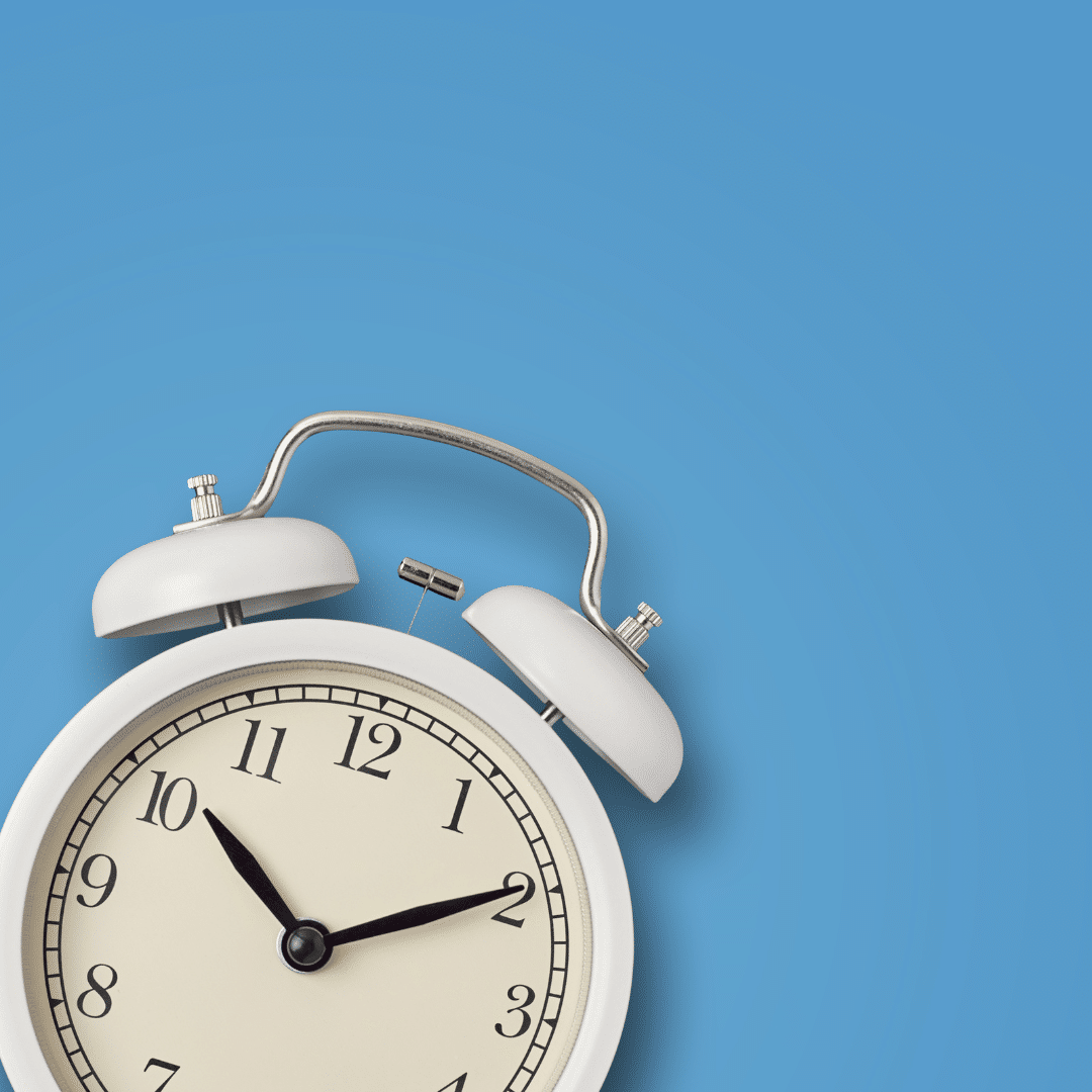 A classic white twin-bell alarm clock showing 10:10 against a solid blue background. The clock features black hour, minute, and second hands with black numerals on a clean, simple face. The background provides a modern contrast.